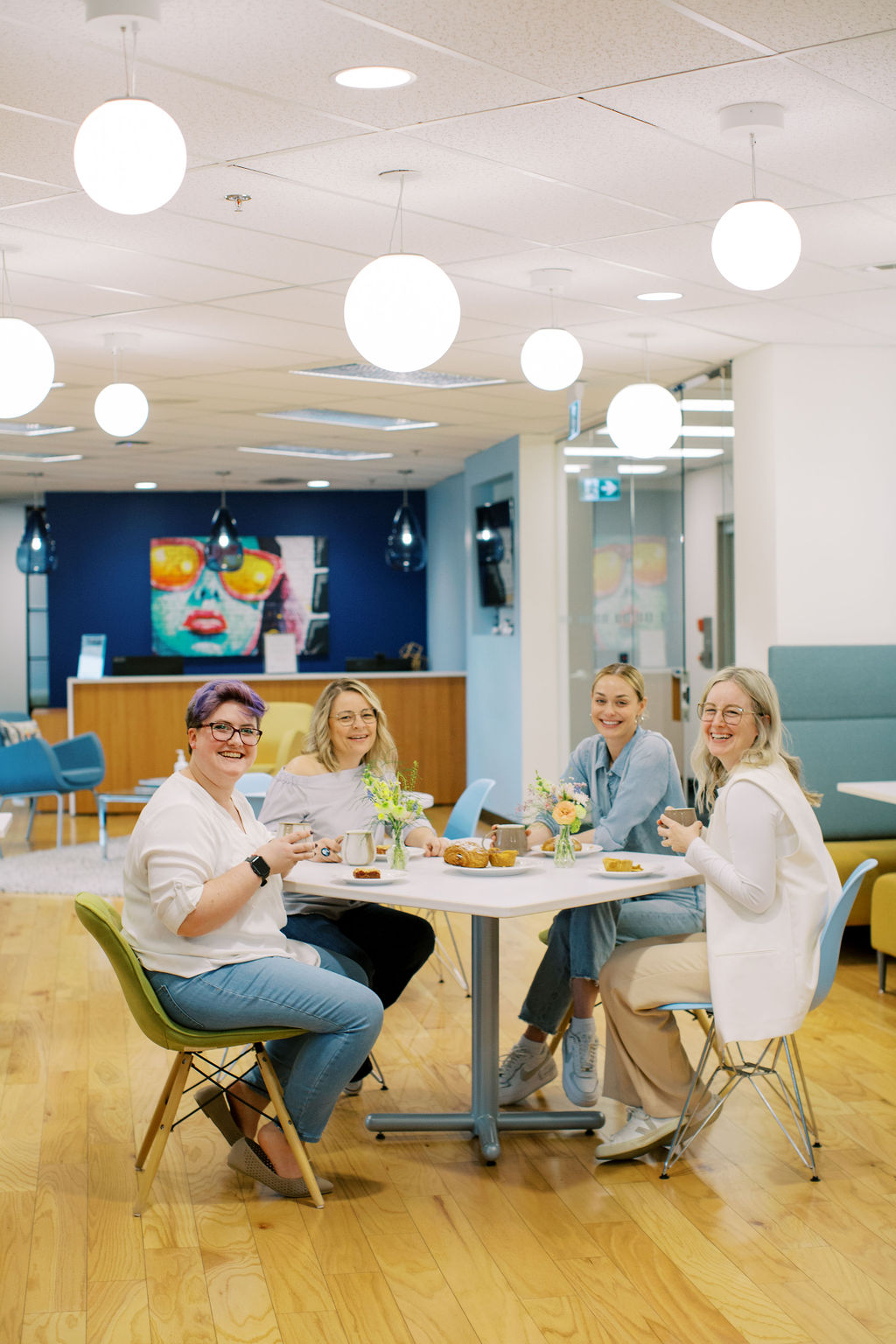 Four people sit at a round table in a modern, bright office space adorned with artwork and overhead lights. A registered psychotherapist and a registered social worker are among them, facilitating an engaging conversation.