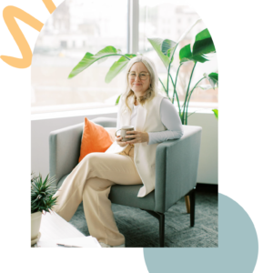 A person with long hair sits in an armchair holding a mug, reflecting on their journey in therapy. Nearby, a plant basks in the natural light streaming through the window, creating a serene setting for counselling and introspection.