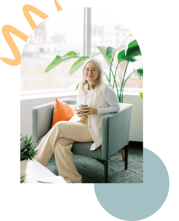 A person with long hair sits in an armchair holding a mug, reflecting on their journey in therapy. Nearby, a plant basks in the natural light streaming through the window, creating a serene setting for counselling and introspection.