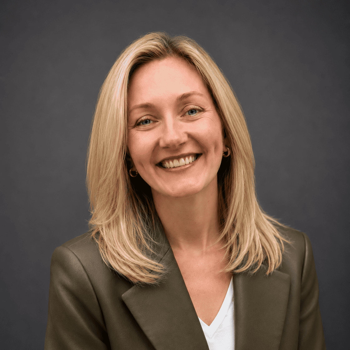 Smiling registered psychotherapist with blonde hair in a dark blazer and white top, posed as if ready to meet you where you are at.